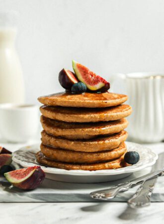 Stack of thick and fluffy oat flour pancakes topped with sliced figs on a small plate.