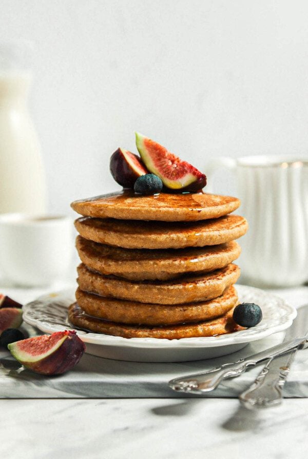 Stack of thick and fluffy oat flour pancakes topped with sliced figs on a small plate.