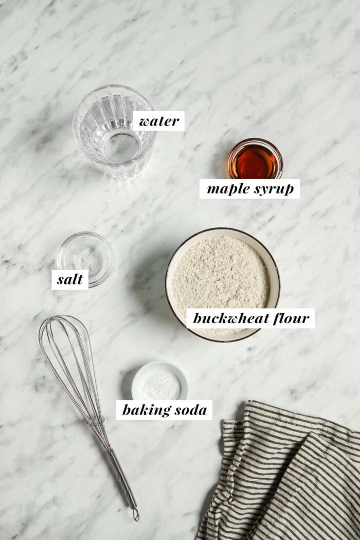 Water, maple syrup, buckwheat flour, salt and baking soda in small bowls. Each ingredient is labelled with a text graphic.