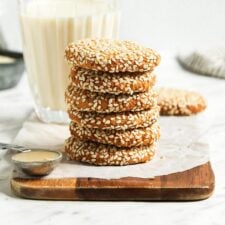 Stack of 5 tahini cookies on a cutting board with a glass of milk behind them.