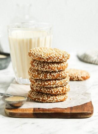 Stack of 5 tahini cookies on a cutting board with a glass of milk behind them.