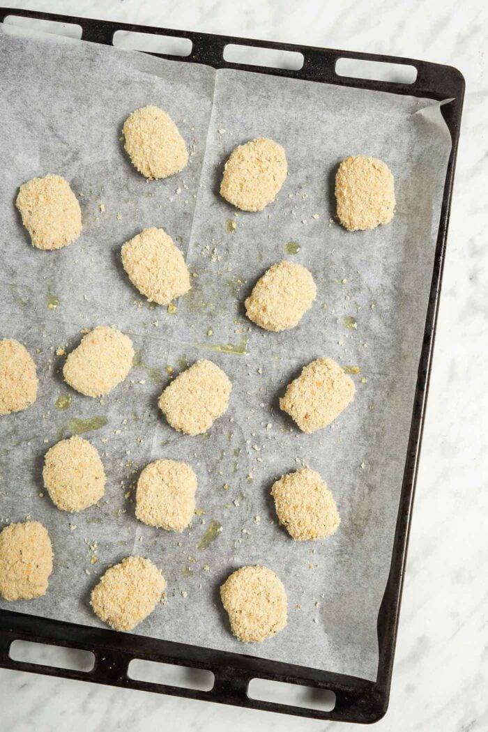 Tofu nuggets coated in bread crumbs on a baking tray before baking.