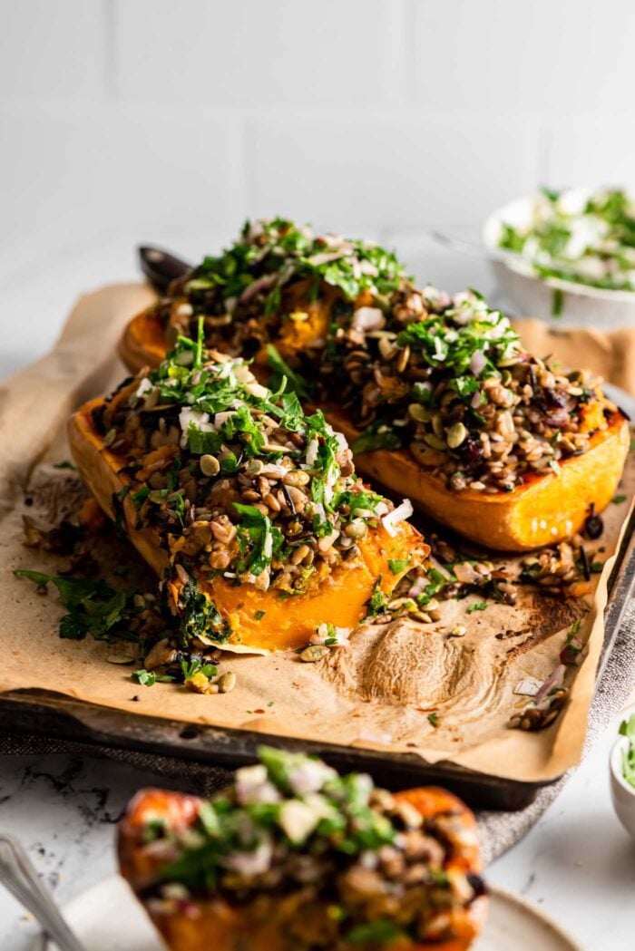 Two large rice, kale and mushroom stuffed butternut squash halves on a baking tray lined with parchment.
