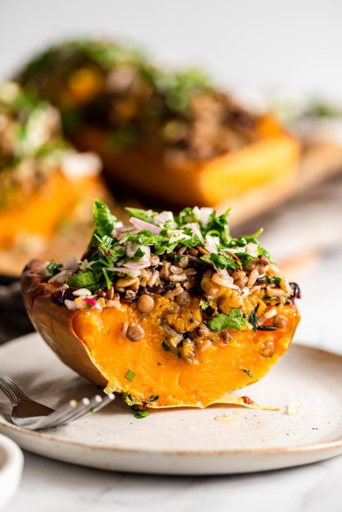 A wedge of sliced stuffed butternut squash on a plate with a fork.