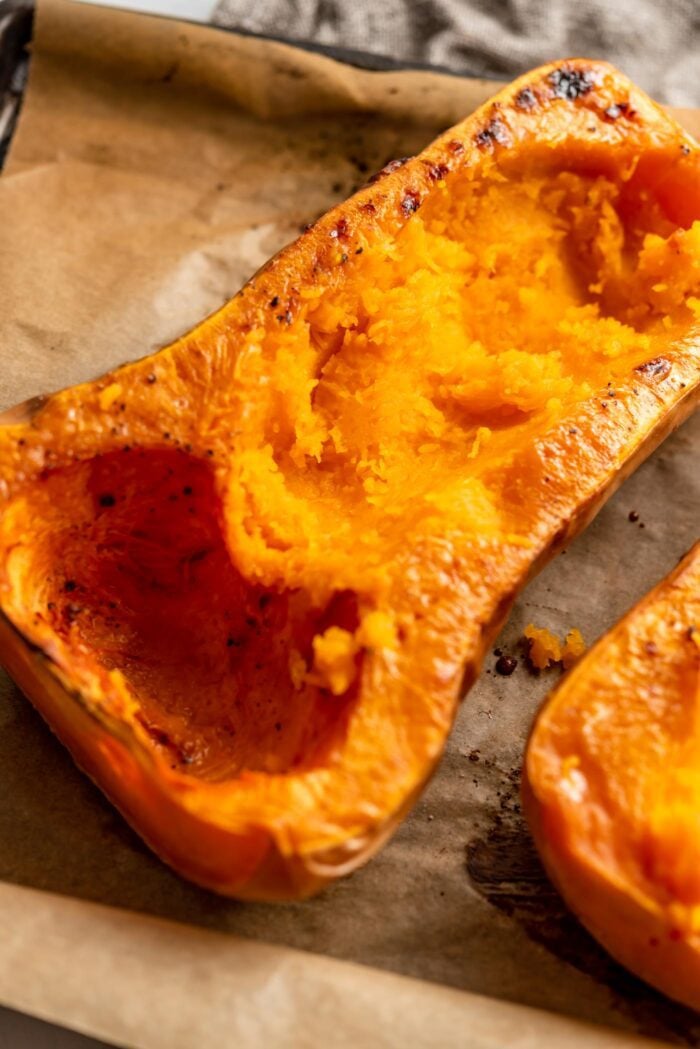 Half of a cooked butternut squash on a roasting pan with some of the flesh scooped out.