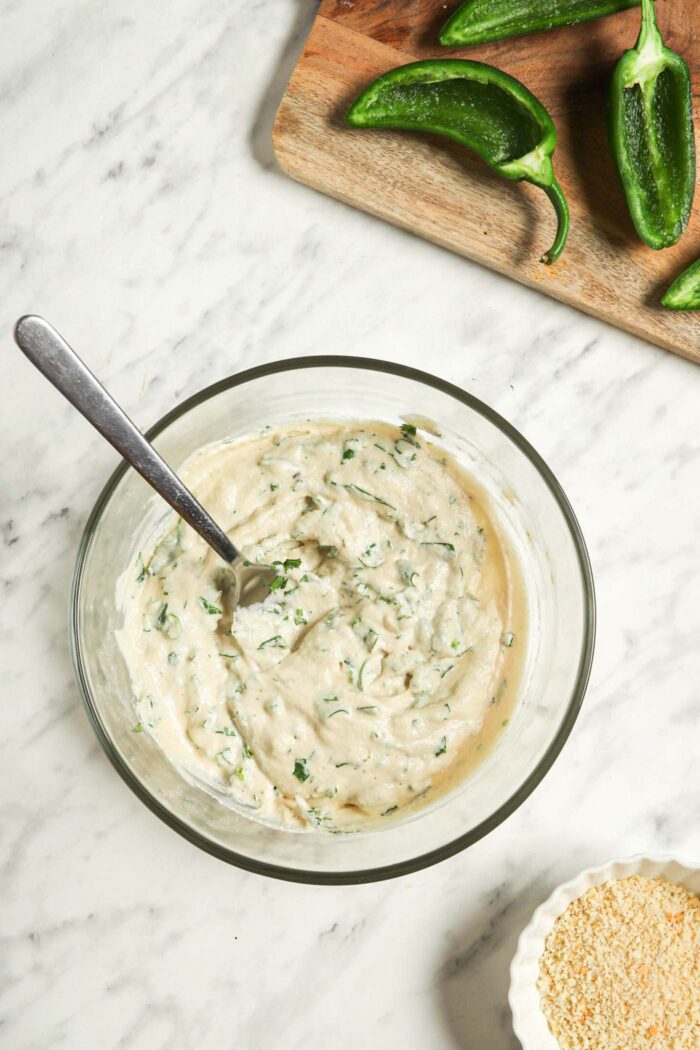 Cashew cream mixed with sliced green onions and cilantro in a glass mixing bowl with a spoon.