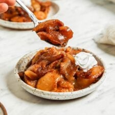 Small spoon taking a spoonful of cinnamon baked apples from a plate.