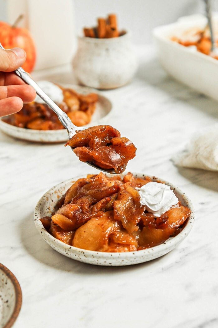 Small spoon taking a spoonful of cinnamon baked apples from a plate.