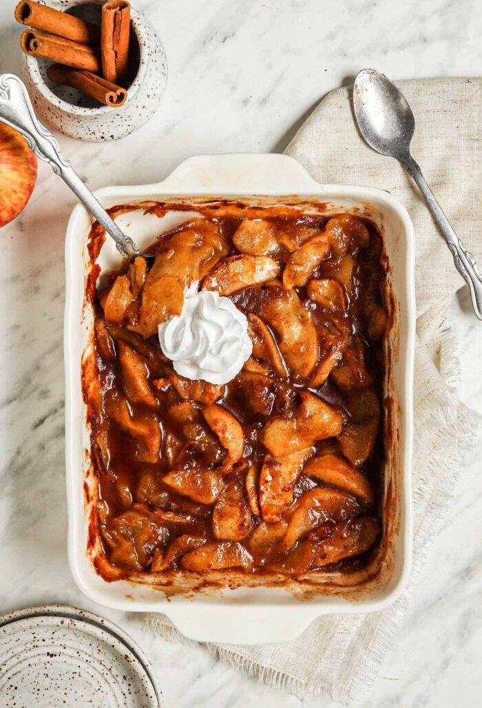Casserole dish of sliced baked apples topped with whipped cream.