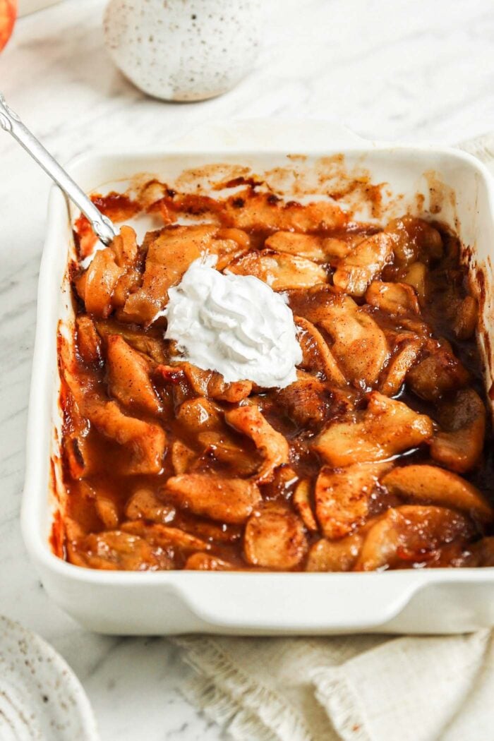 Casserole dish of sliced baked apples topped with whipped cream.