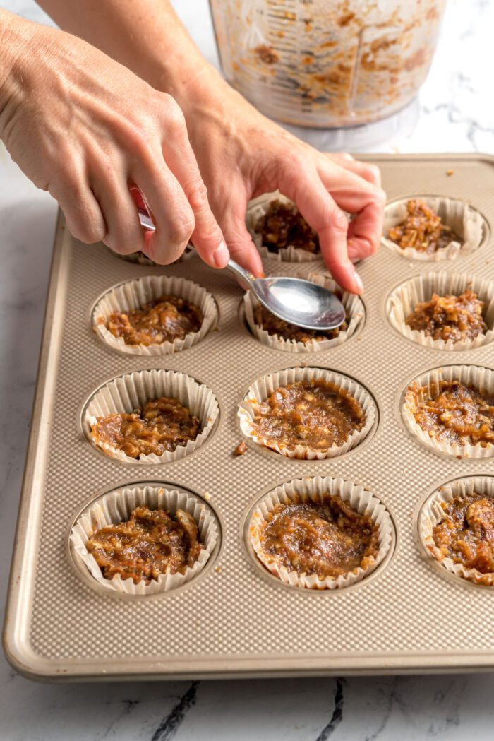 Using a spoon to smooth pecan pie filling in mini tarts made in a muffin pan.