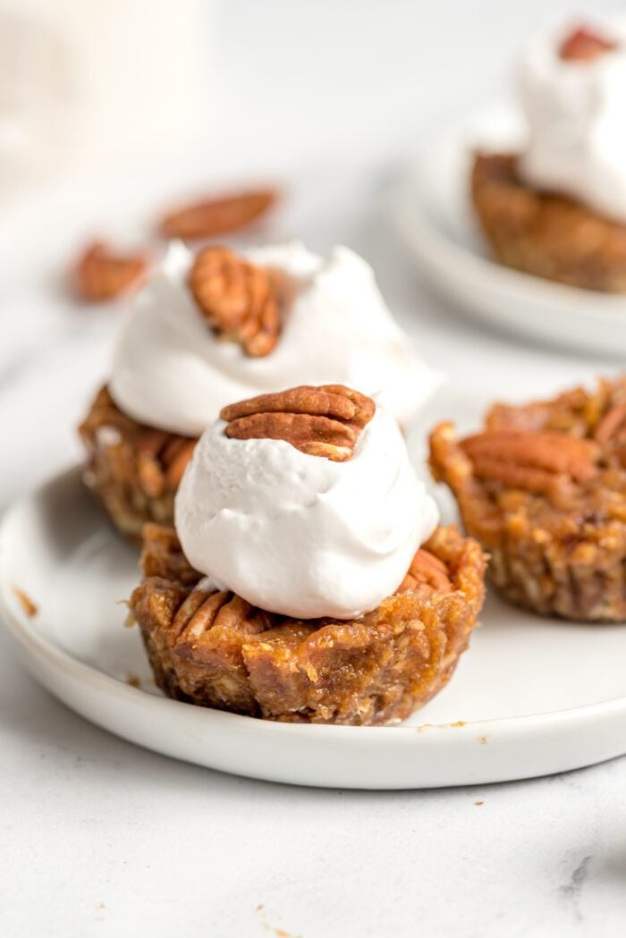 A mini pecan pie tart topped with whipped cream and a pecan on a plate.