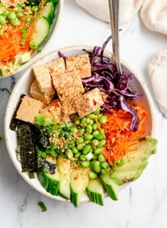 Overhead view of a vegan tofu poke bowl with carrot, avocado, carrot, cabbage, edamame, sesame seeds and cucumber.