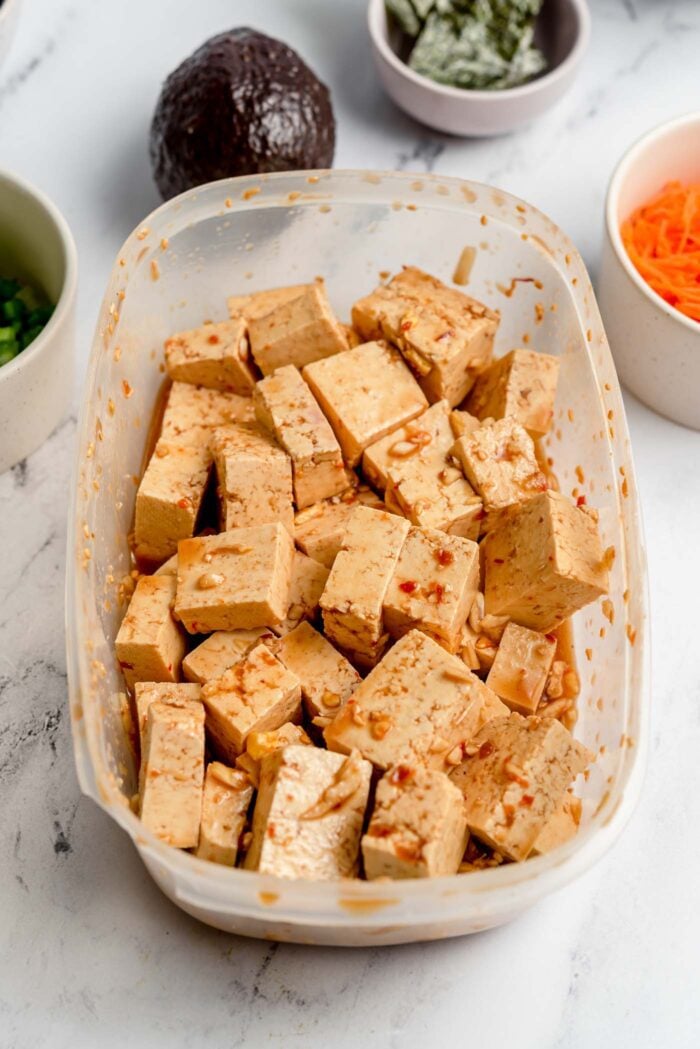 Tofu cortado en cubitos marinado en salsa de soja y jengibre en un recipiente Tupperwear.
