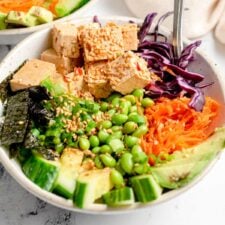 Colorful tofu poke bowl with carrot, cabbage, cucumber, avocado, nori and edamame.