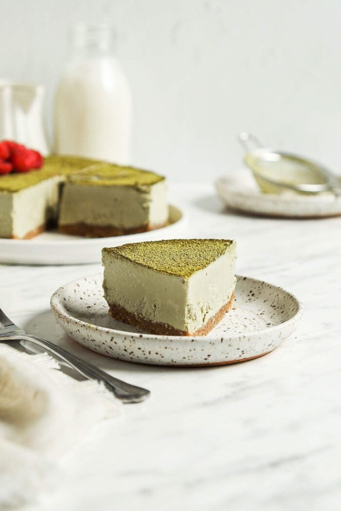 Slice of vegan no-bake matcha cheesecake on a plate with a fork resting on it.