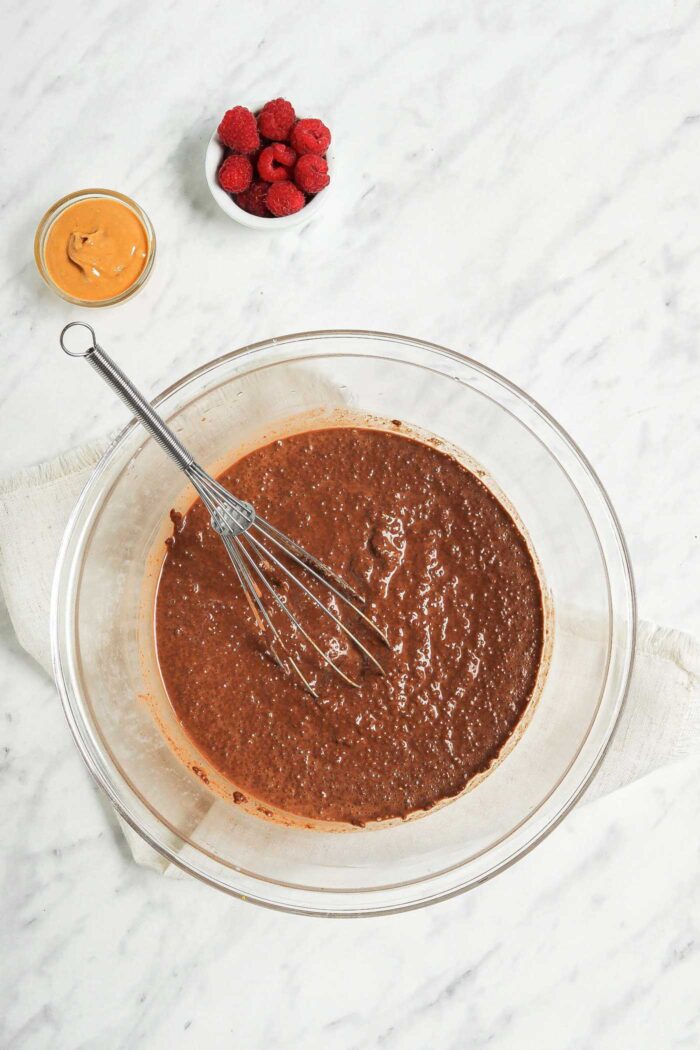 Large glass mixing bowl of chocolate chia pudding with a whisk in it.