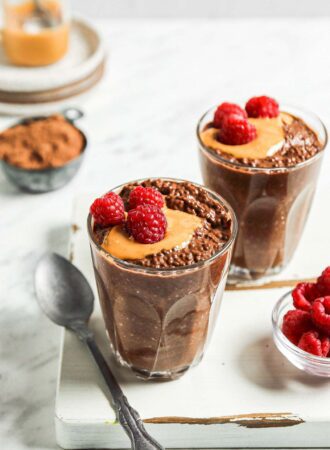 Two bowls of chocolate chia seed pudding topped with peanut butter and fresh raspberries.