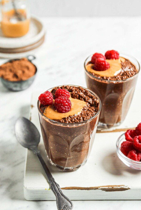 Two bowls of chocolate chia seed pudding topped with peanut butter and fresh raspberries.