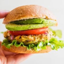 Hand holding a chickpea veggie burger on a bun with lettuce, tomato, onion and avocado.