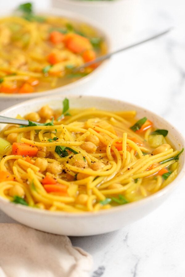 Two bowls of vegan chicken noodle soup with vegetables and spaghetti noodles.