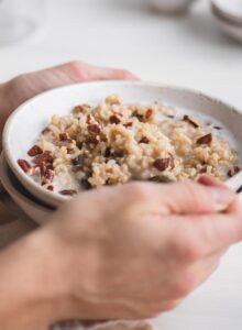 Hand using a spoon in a bowl of brown rice pudding with raisins and coconut milk.