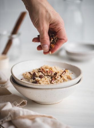 Sprinkling chopped pecans over a bowl of brown rice pudding with raisins and coconut milk.