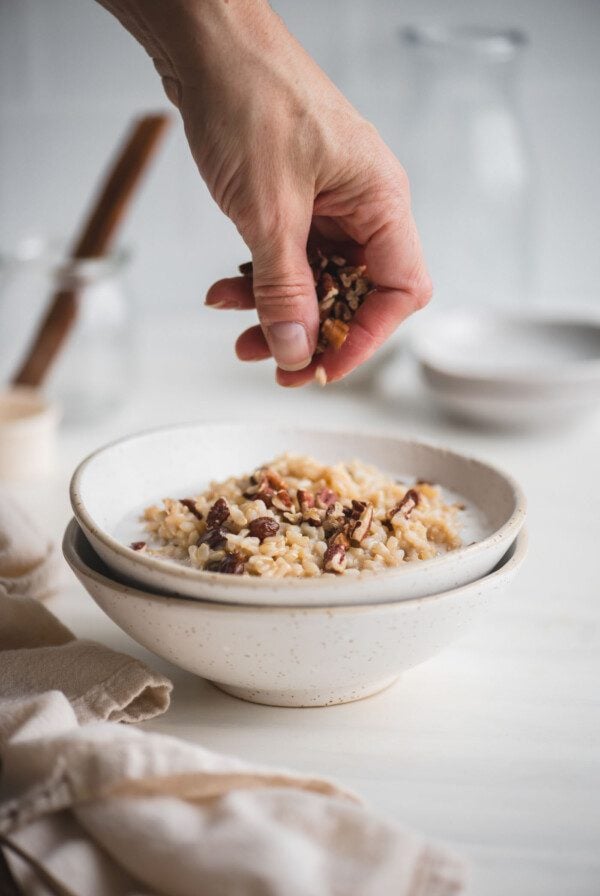 Sprinkling chopped pecans over a bowl of brown rice pudding with raisins and coconut milk.