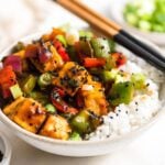 Close up of a bowl of sweet and sour tofu stir fry with rice and sesame seeds.