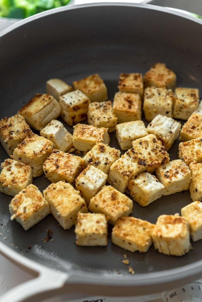 Tofu cortado en cubitos crujiente cocinando en una sartén.