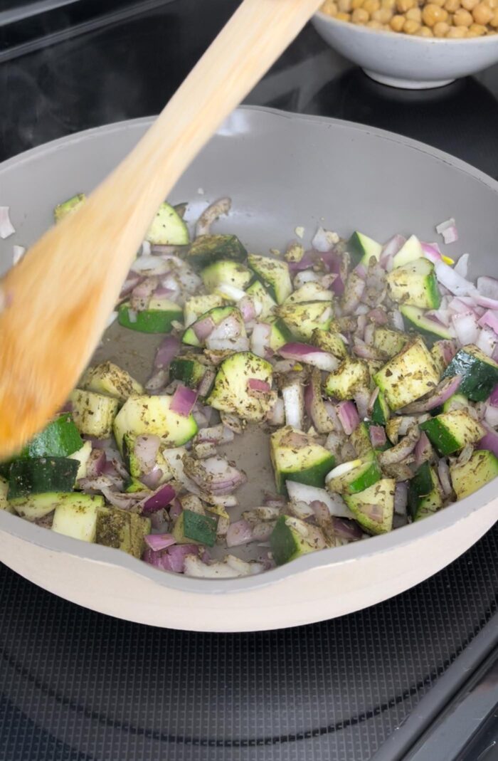 Chopped onion and zucchini with herbs cooking in a skillet on the stovetop.