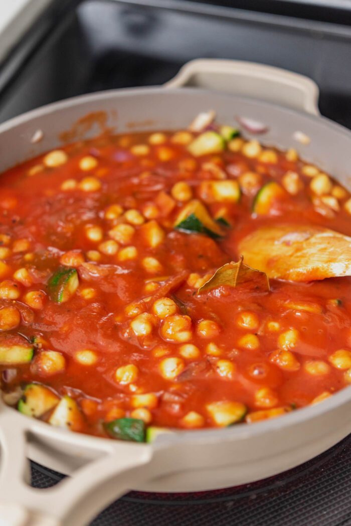 Chickpeas cooking in a tomato sauce in a skillet on the stovetop.