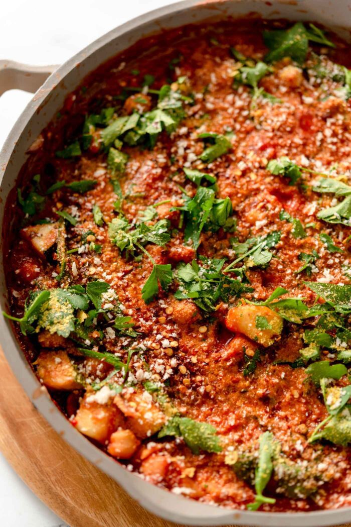 Overhead view of a tomato chickpea stew topped with parsley and breadcrumbs in a skillet sitting on a cutting board.