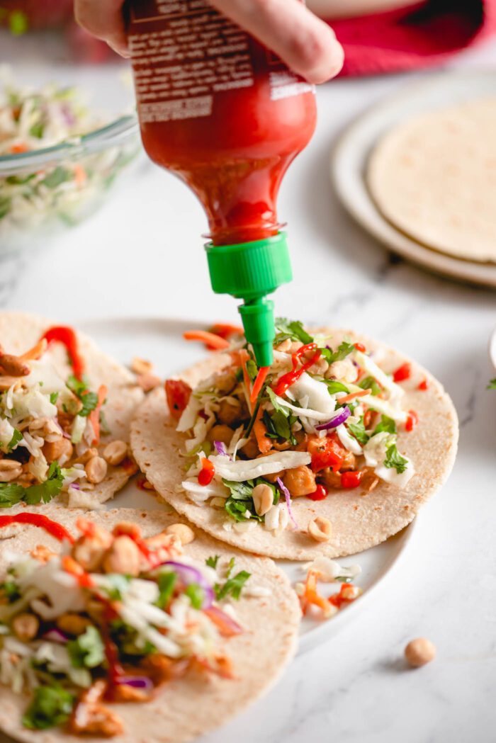 Adding Sriracha to a chickpea and cabbage slaw taco on a plate.