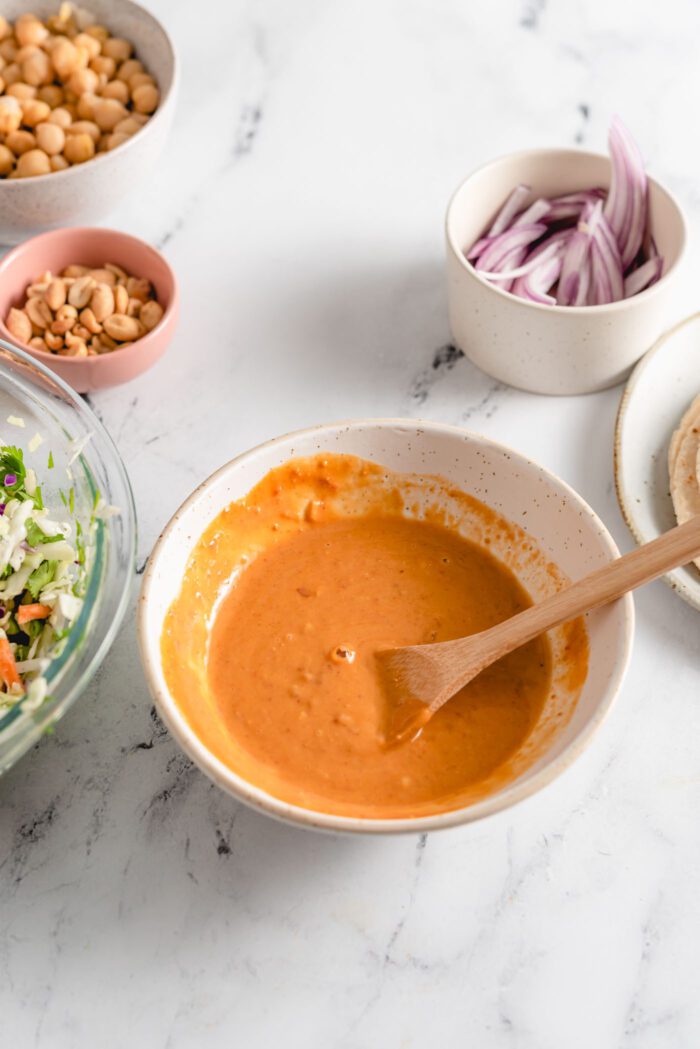 Creamy peanut sauce in a small bowl with a wooden spoon.