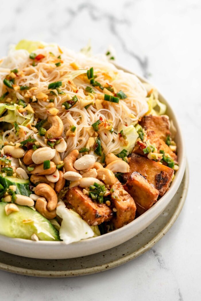 Close up of a vermicelli salad with cashews, lettuce, cucumber and tofu.