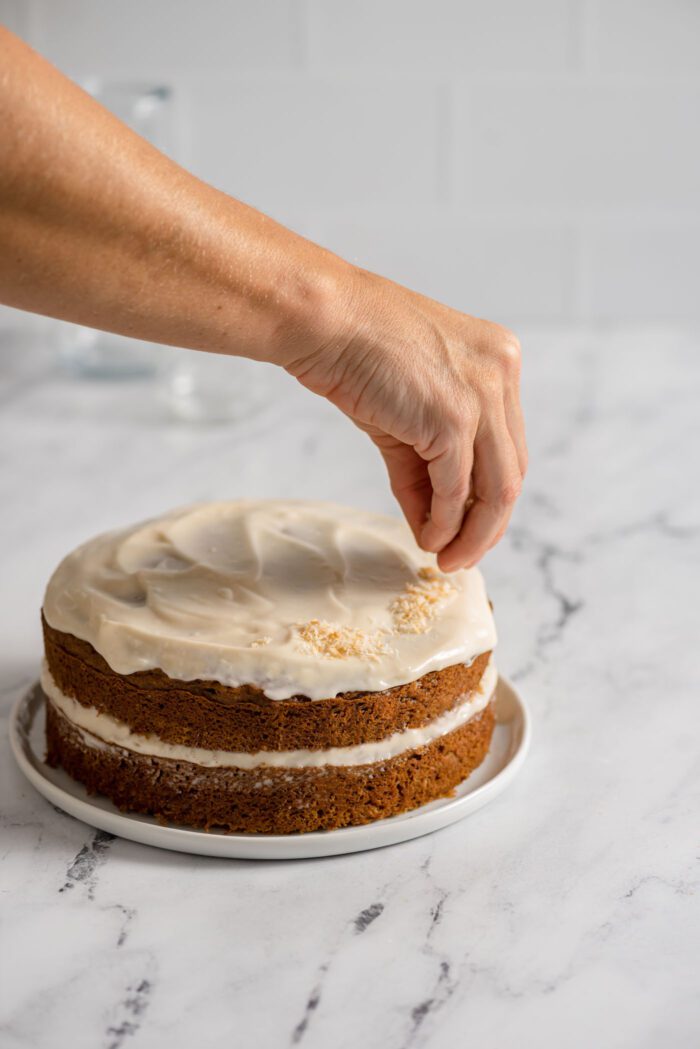 Sprinkling toasted coconut on top of a round carrot cake.