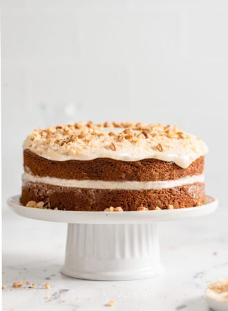 Straight on view of a double-layered carrot cake topped with cream cheese frosting, coconut and walnuts.