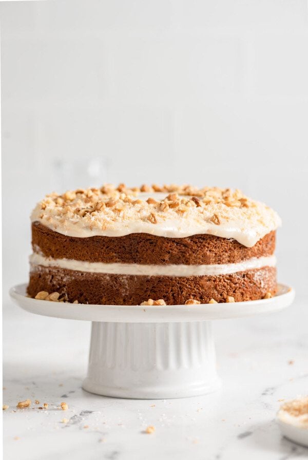 Straight on view of a double-layered carrot cake topped with cream cheese frosting, coconut and walnuts.