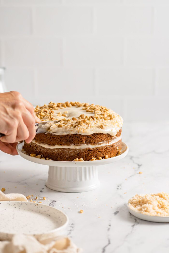 Cutting a slice of carrot cake from a double layered cake on a cake stand.