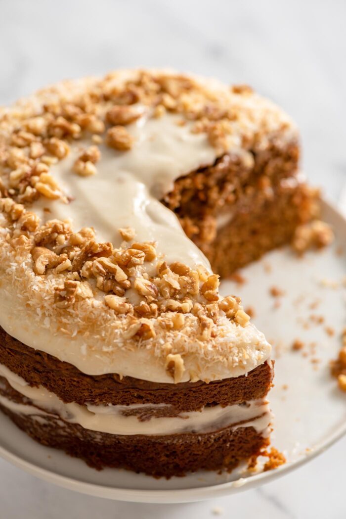 Double layered carrot cake topped with coconut and walnuts. A large slice has been cut from it.