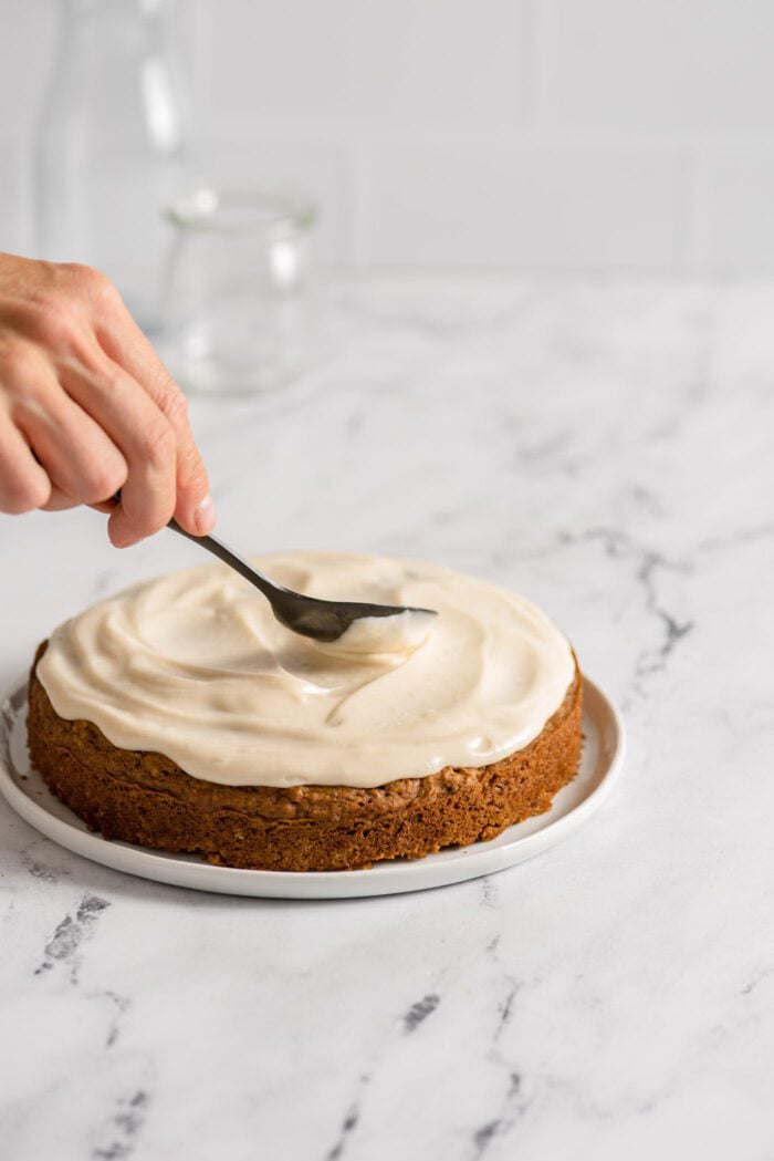Spreading cream cheese frosting on a round carrot cake.
