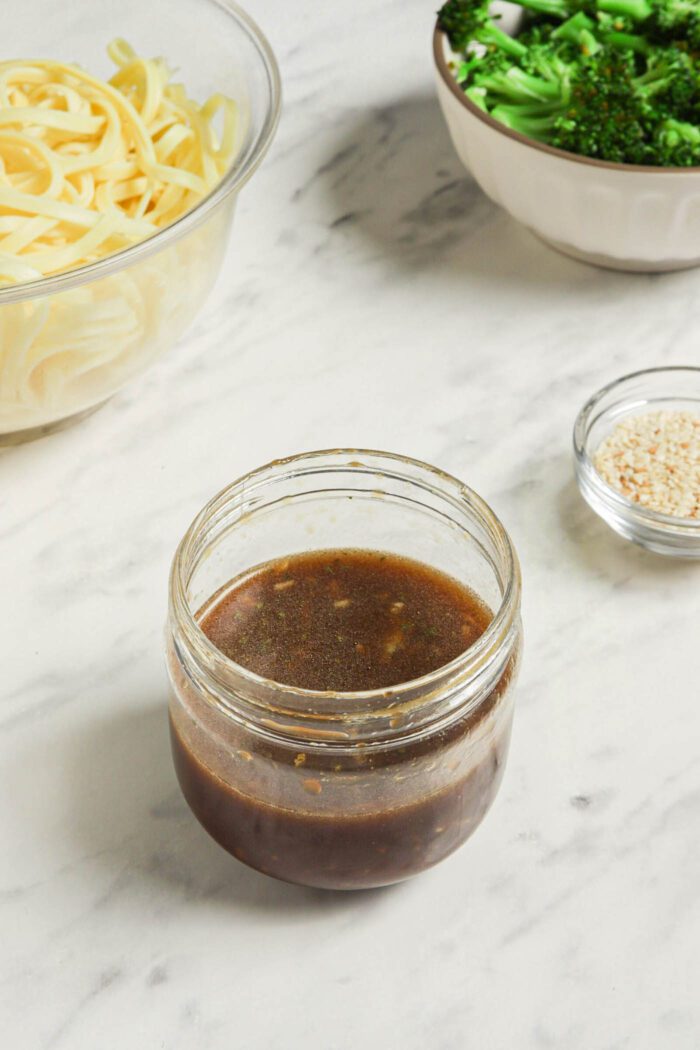 Small jar of a dark sauce on a marble surface.