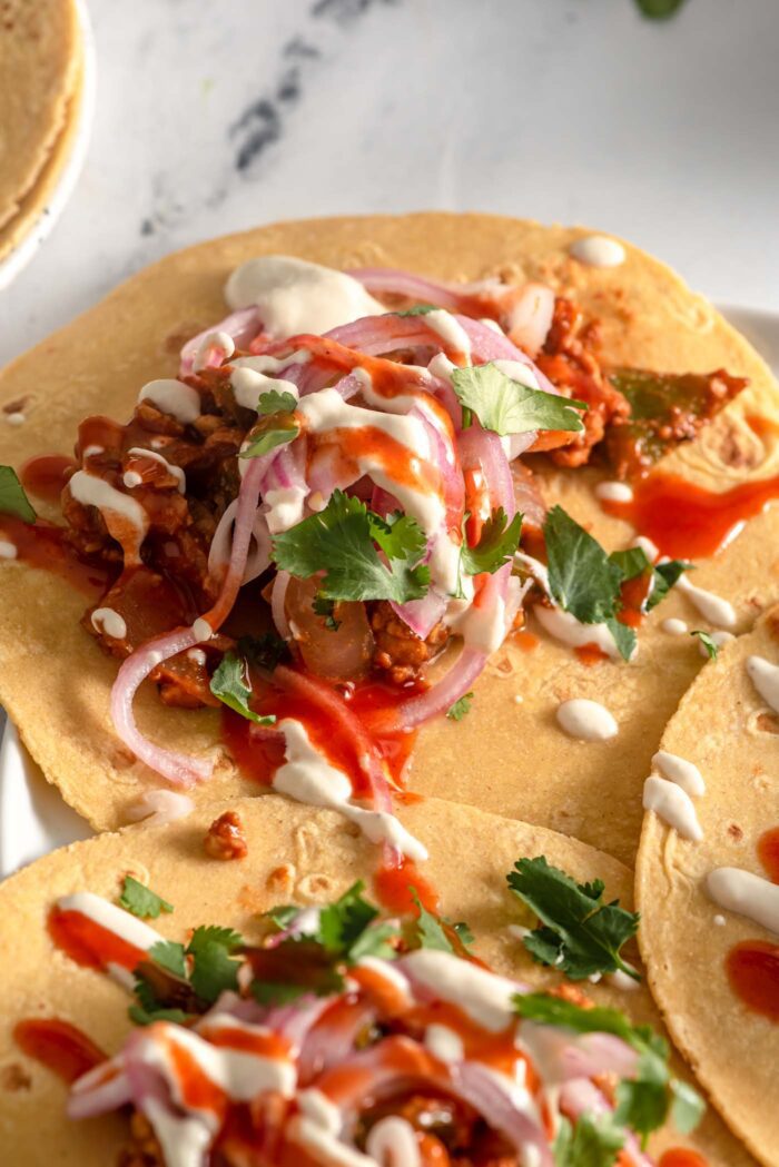 3 tempeh tacos with pickled red onion and cashew cream sauce on a plate.