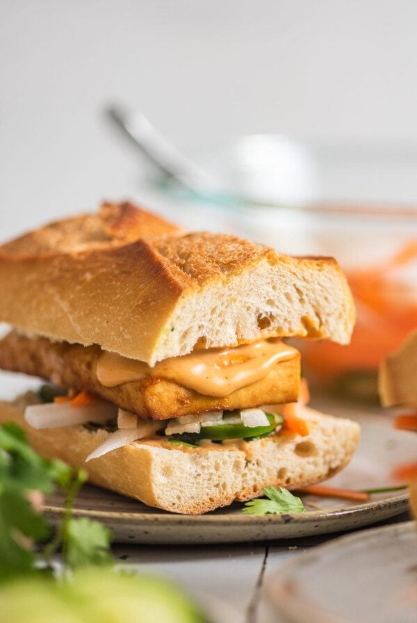 Close up of a tofu bahn mi sandwich with spicy mayo and pickled veggies on a plate.