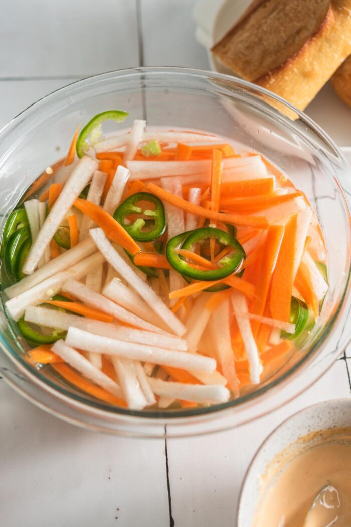 Pickled carrot, daikon and jalapeno in a glass bowl.