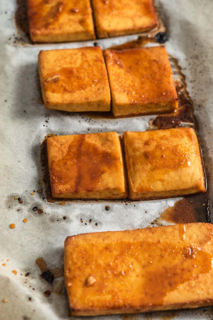 Thick slices of baked tofu coated in marinade on a baking tray.