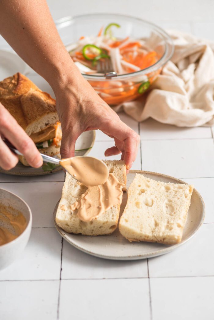 Using a spoon to spread spicy mayo sauce on a toasted baguette.