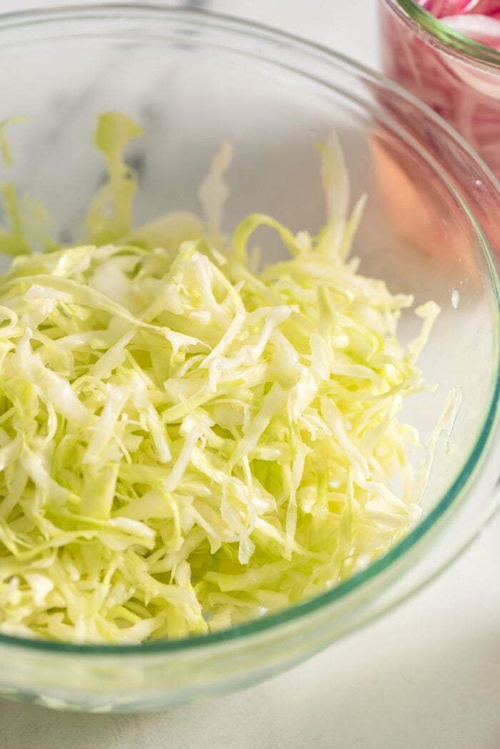 Thinly sliced green cabbage in a glass bowl.