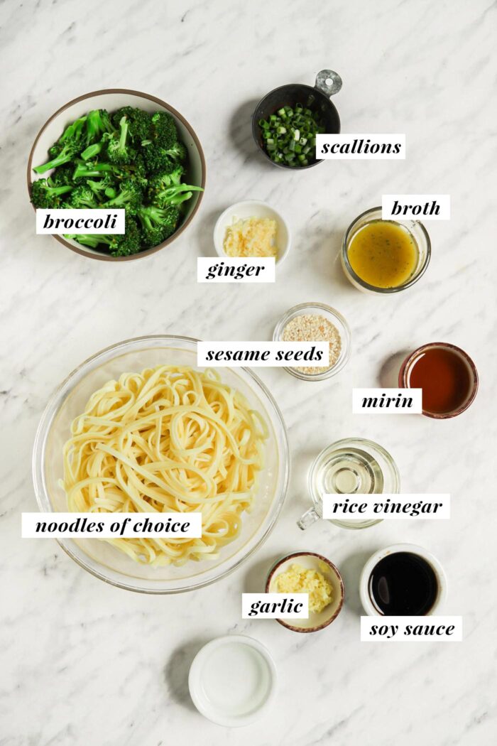 All the ingredients needed for making a sesame noodle recipe in small bowls on a counter top. Each ingredient is labelled with text and the recipe appears in the recipe card on the page.